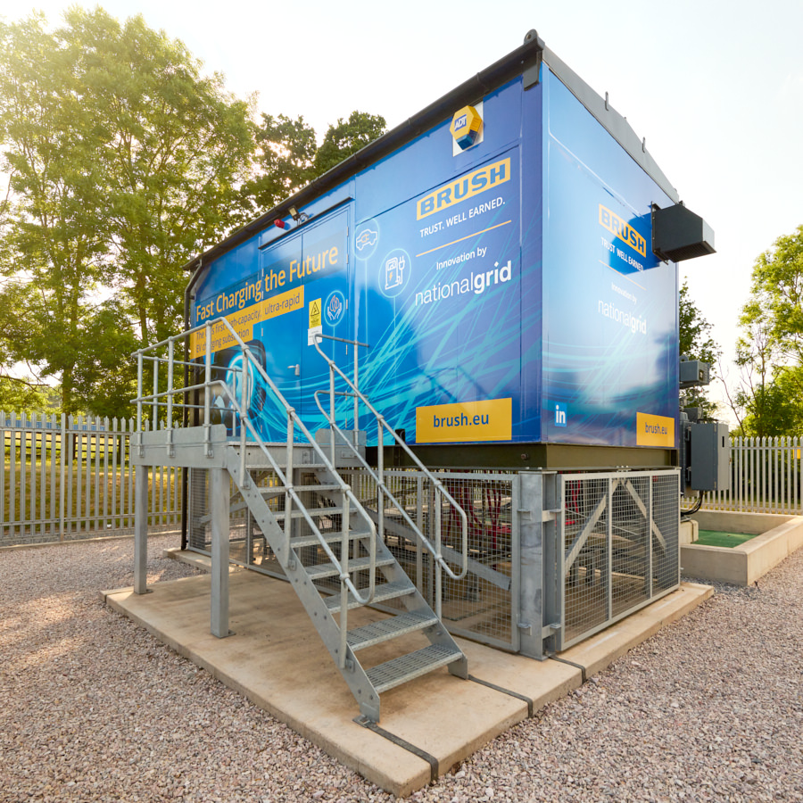 Outdoor fast-charging/energy enclosure with steel access stairs at a utility site, branded BRUSH and National Grid