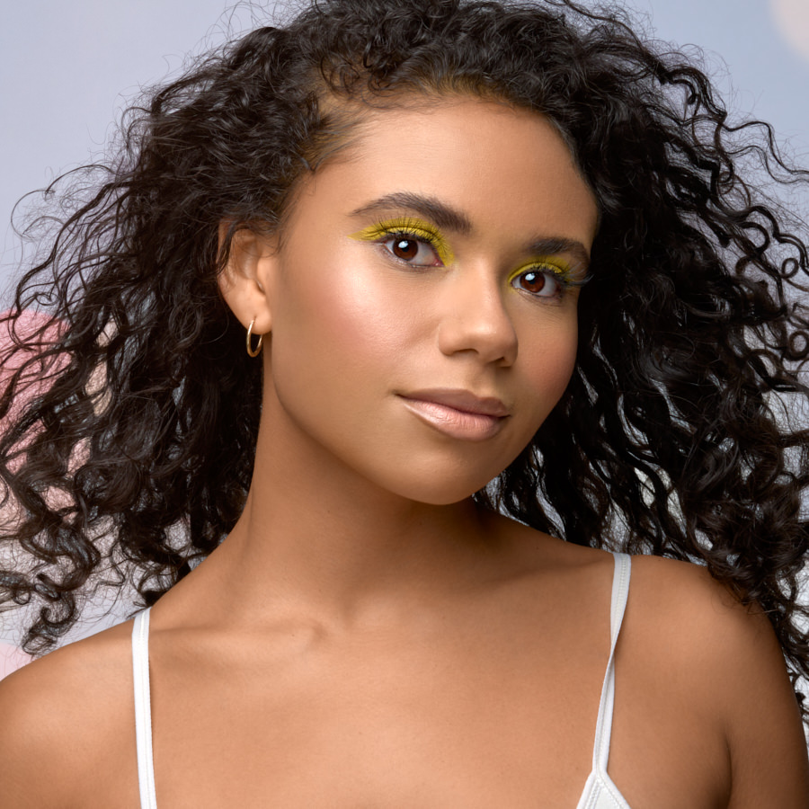 Beauty portrait with vibrant yellow eye makeup and curly hair under soft studio lighting