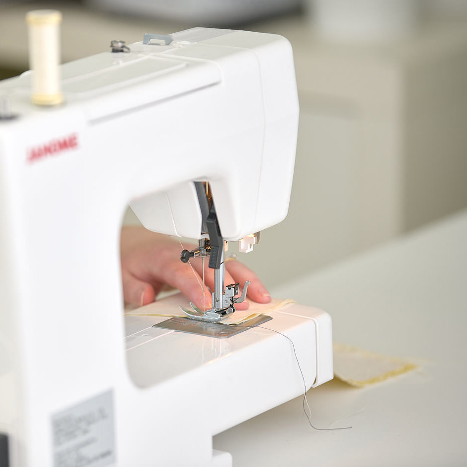 Close-up of a sewing machine stitching fabric, operator’s hand guiding the material